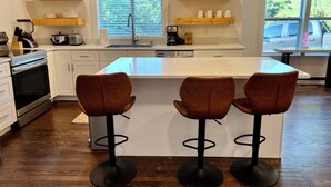 Una cocina moderna con una isla central, taburetes de bar, estantes de madera y un ventanal con vistas.