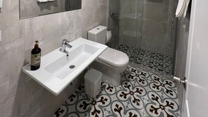 A modern bathroom with a white sink, a toilet, a glass shower enclosure, and patterned floor tiles.