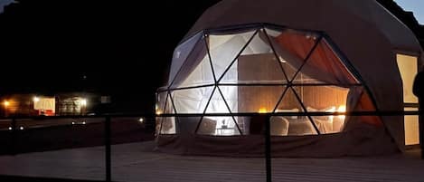 A dome-shaped tent with a fire inside, surrounded by a wooden deck and a metal railing.