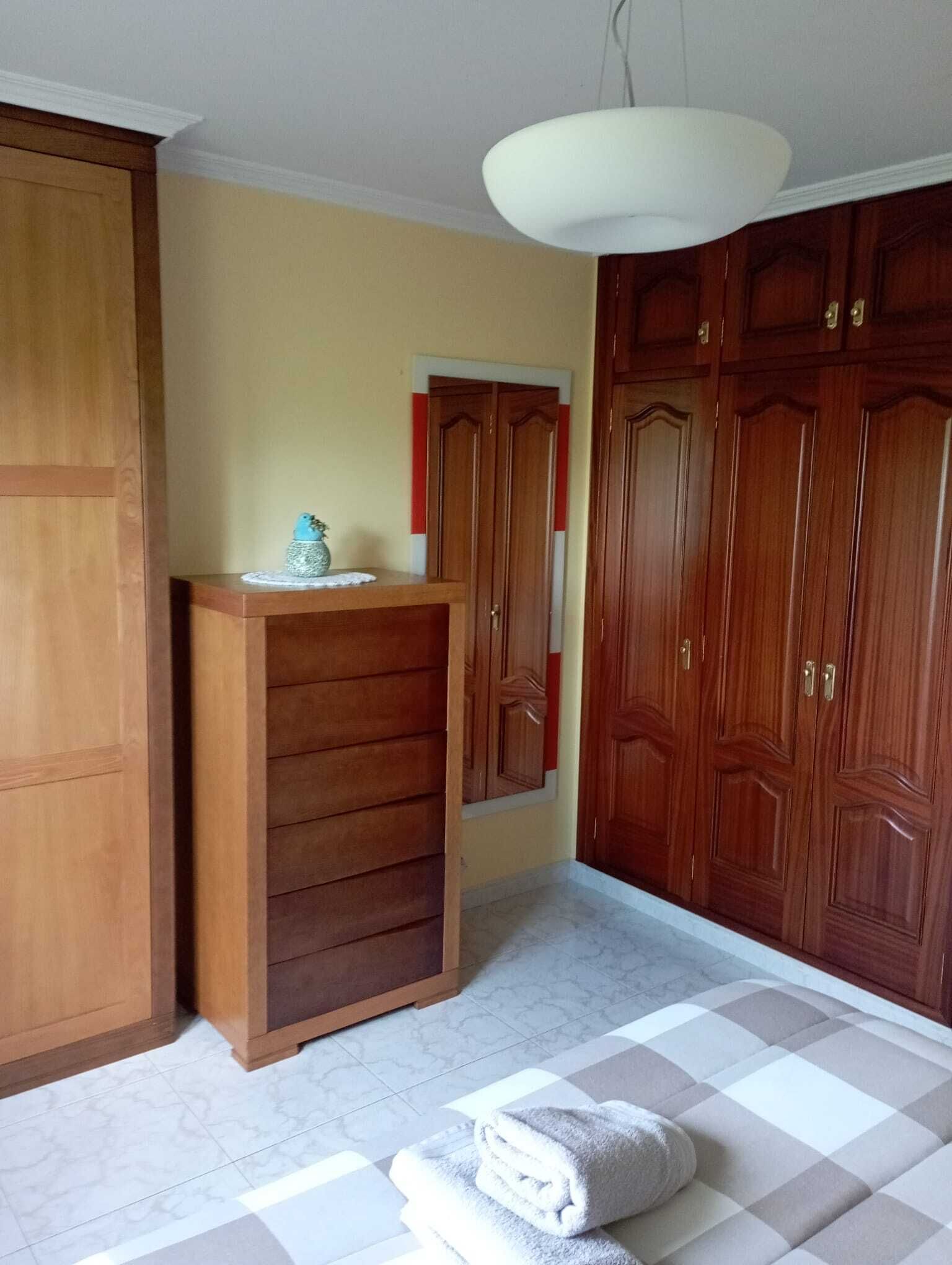 Une pièce avec une armoire en bois, une petite table ornée d’un objet décoratif et un sol à carreaux.