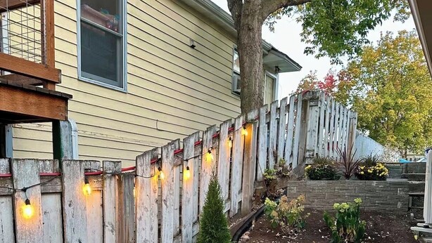 An outdoor patio with a table and chairs, a wooden fence, and string lights. - Centrally Located Basement Apartment, Newly Remodeled, Pets Welcome (Missoula)
