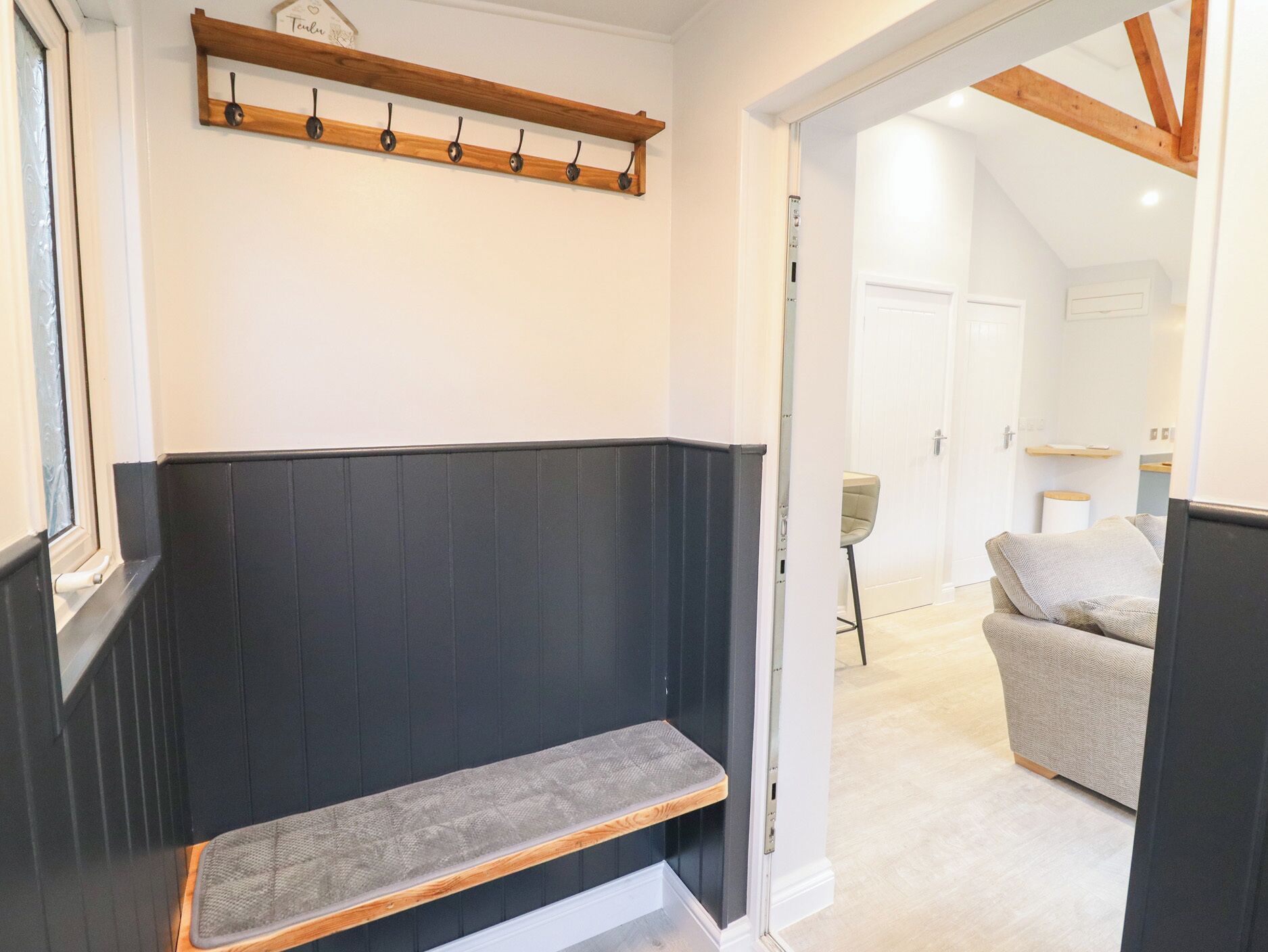 A modern interior with a bench, a coat rack, and a doorway leading to another room.