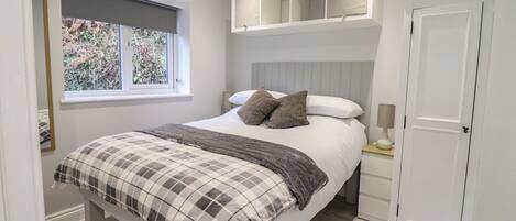 A bedroom with a bed, a window, a bedside table, and a wardrobe.