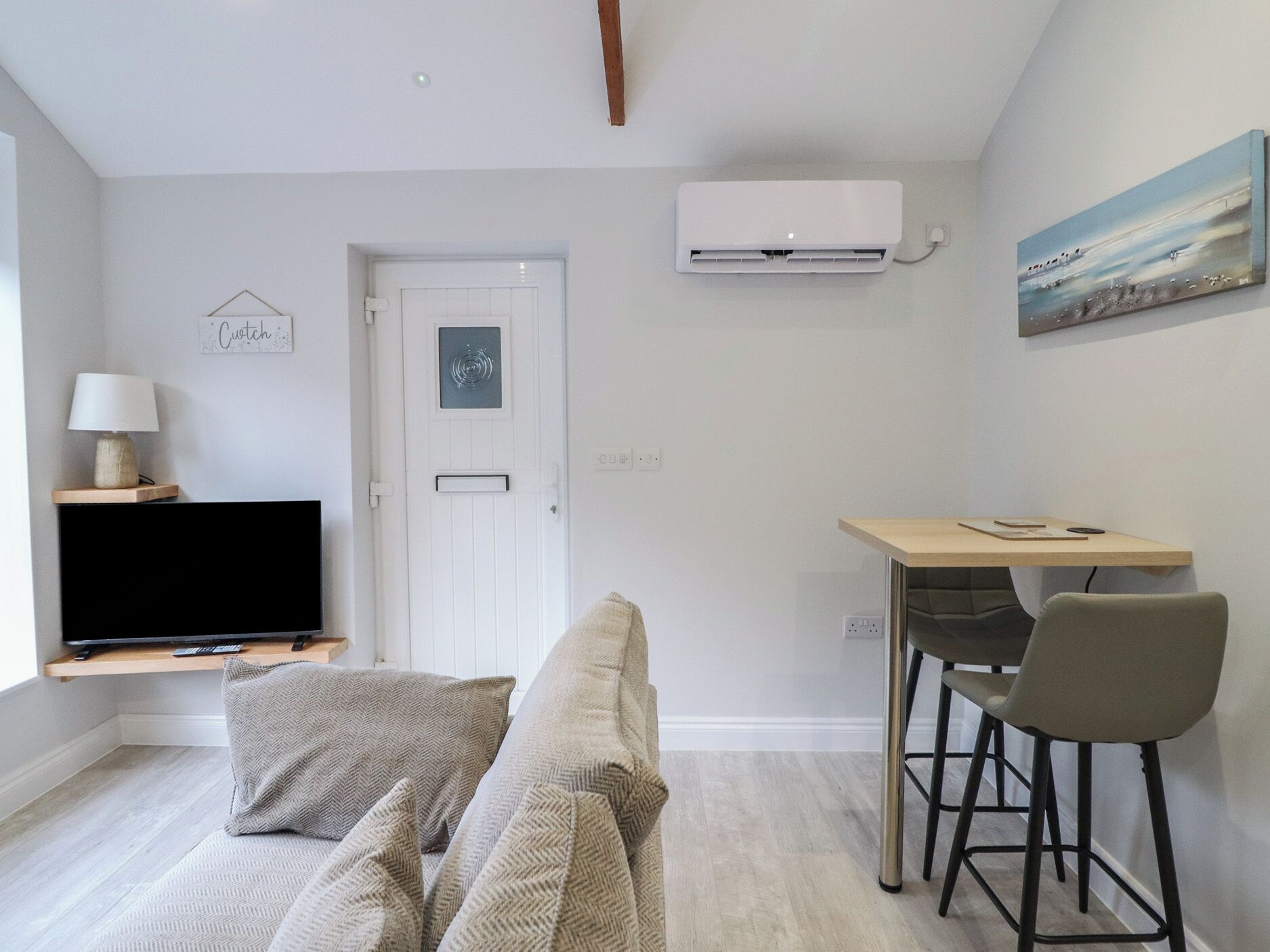 A modern living room with a sofa, a TV, a desk with a chair, an air conditioner, and a painting on the wall.
