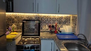 Uma cozinha com armários brancos, fogão a gás, pia e azulejos de revestimento estampados.