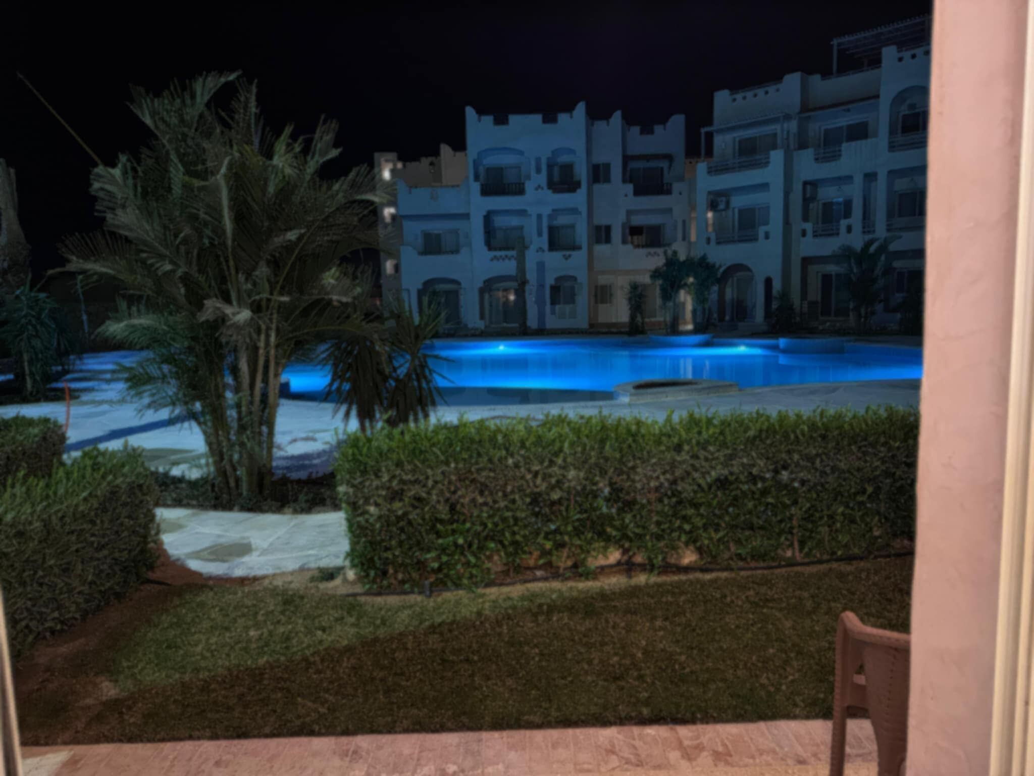 Vista noturna de um hotel com piscina, palmeiras e um jardim bem cuidado.