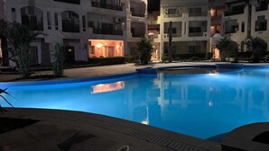 Uma área de piscina à noite, com um edifício ao fundo.