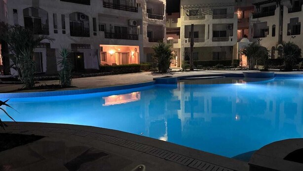 Une piscine éclairée la nuit, avec un bâtiment visible en arrière-plan.