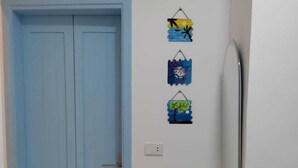 Quarto com porta azul, interruptor de luz fixado na parede e três decorações penduradas.