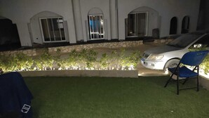 Une terrasse dallée avec une petite pelouse, une voiture blanche et une chaise bleue.