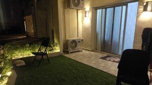 Un espace patio avec un revêtement de sol en gazon synthétique, une chaise, un appareil de climatisation et une porte-fenêtre coulissante.