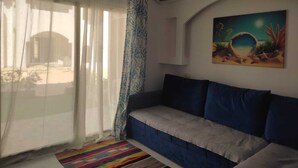 Un salon comprenant un canapé, un tapis coloré, un tableau représentant une scène de plage et un appareil de climatisation.