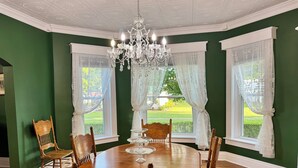 Un comedor con una mesa redonda de madera, seis sillas, una araña y ventanas amplias con cortinas blancas.