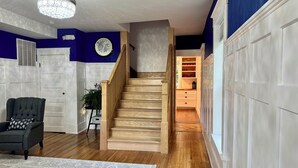Una escalera que conduce a un armario con estantes, una silla, una planta y una lámpara en el techo.