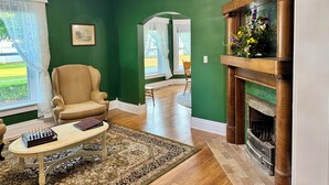 Una habitación con pared verde, chimenea de madera, un tablero de ajedrez sobre una mesa y una silla.