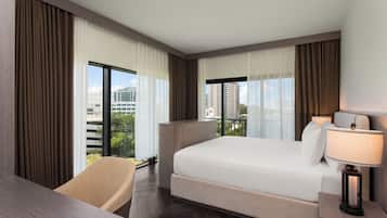 Une chambre d’hôtel équipée d’un lit, d’un bureau, d’une chaise, d’une lampe et de grandes fenêtres avec des rideaux.