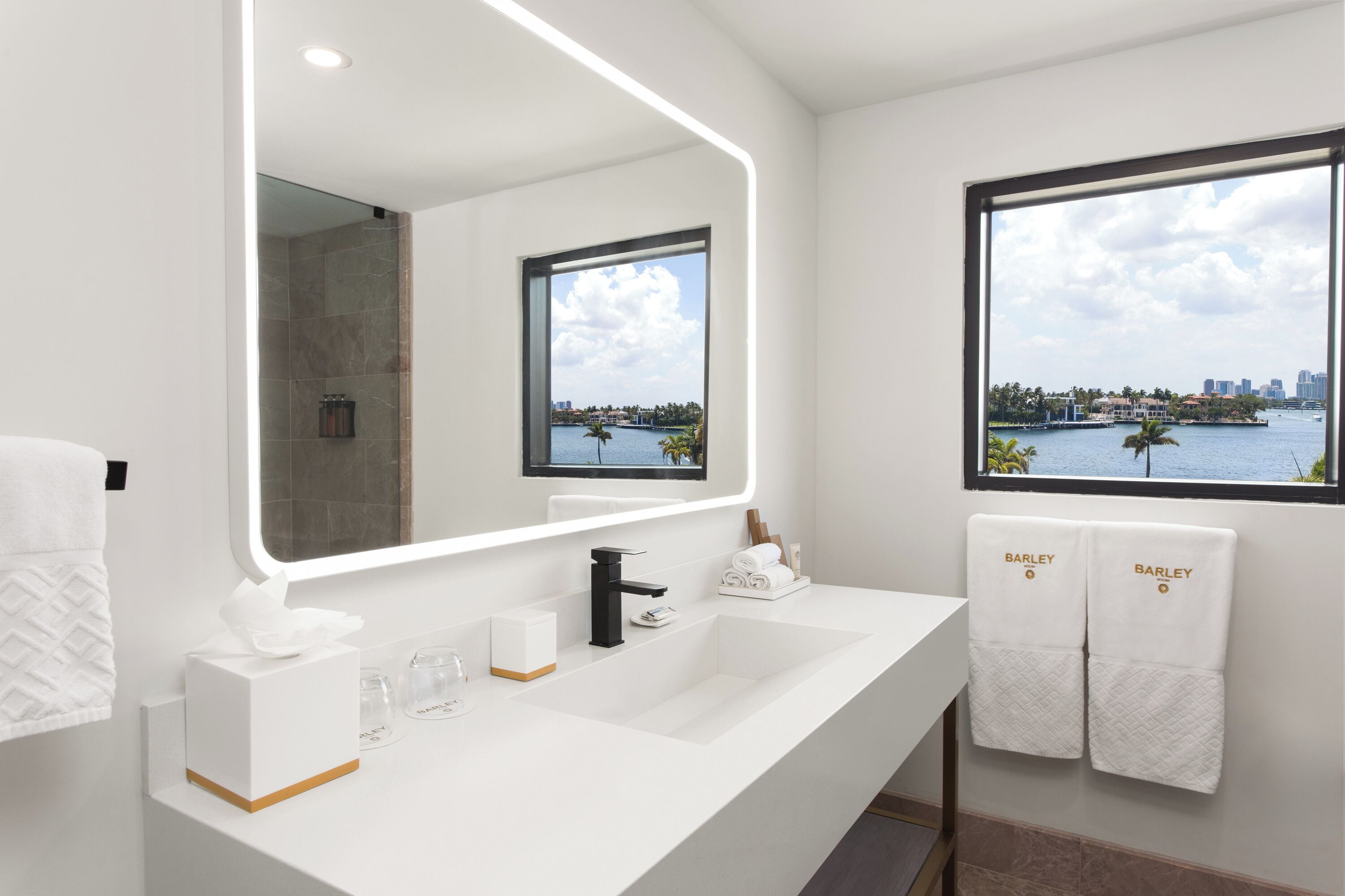 Un baño moderno con un espejo grande, un lavamanos blanco y un ventanal con vistas a la ciudad.