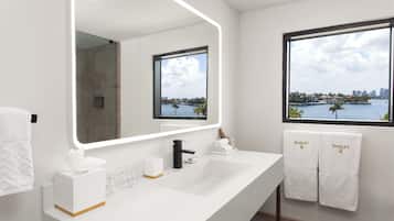 Un baño moderno con un espejo grande, un lavamanos blanco y un ventanal con vistas a la ciudad.