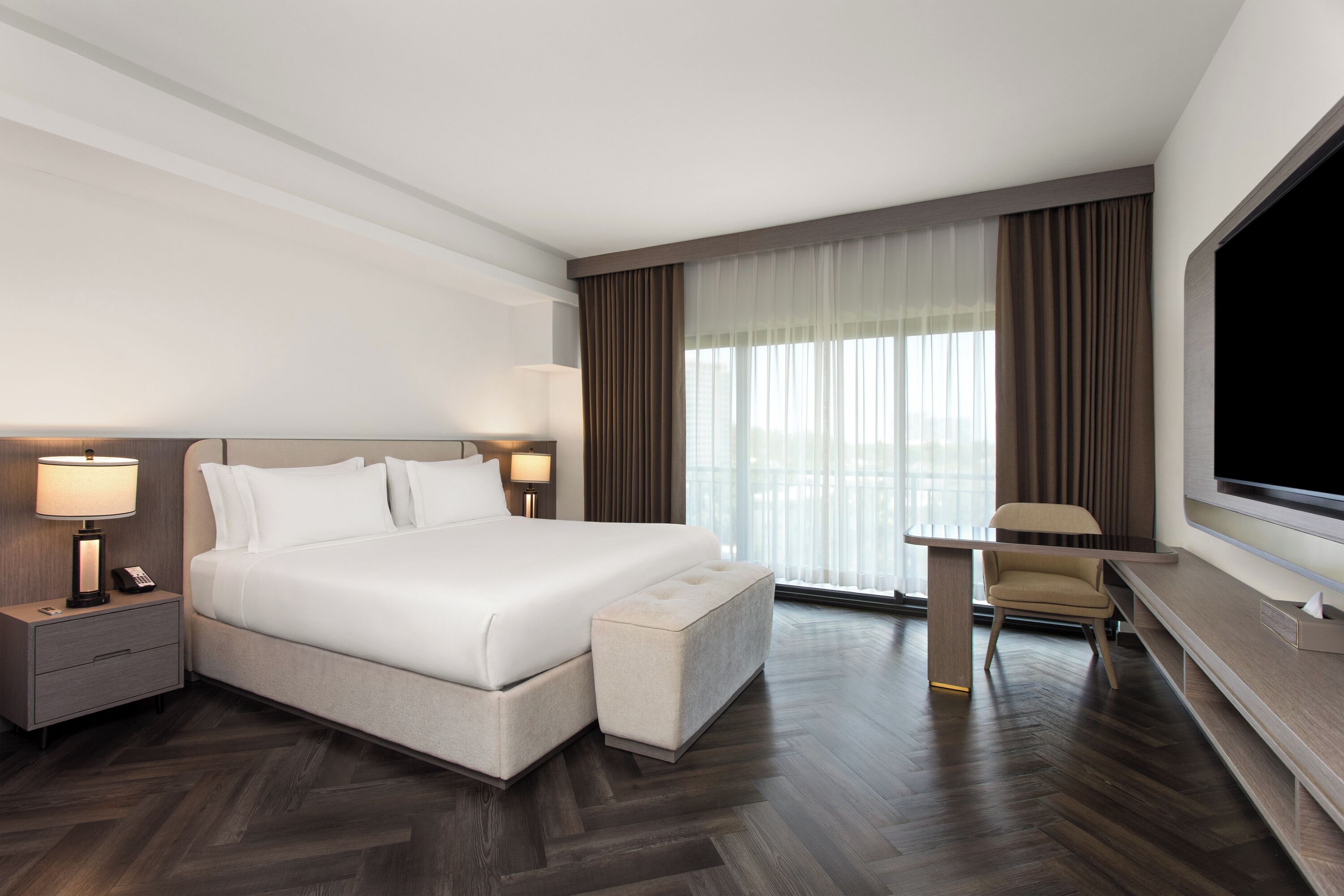 A hotel room with a large bed, bedside lamps, a desk with a chair, and a TV.