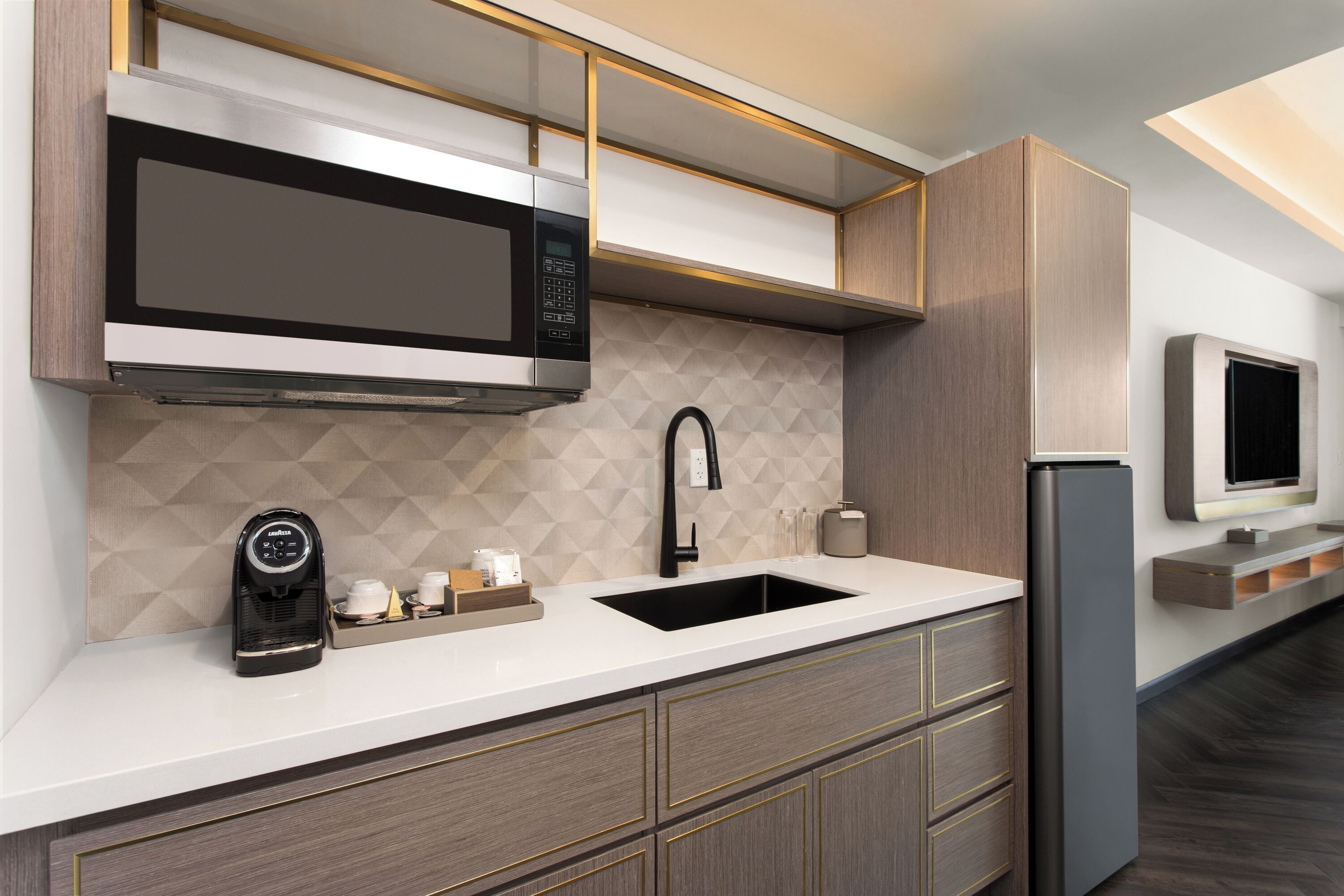 A modern kitchen with a built-in microwave, a coffee machine, a sink, and a refrigerator.