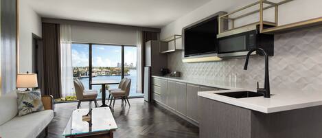 Een moderne hotelkamer met een eethoek, een keuken met een magnetron, en uitzicht op een waterpartij.