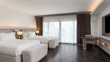 A hotel room with two beds, a desk, a chair, and a TV.