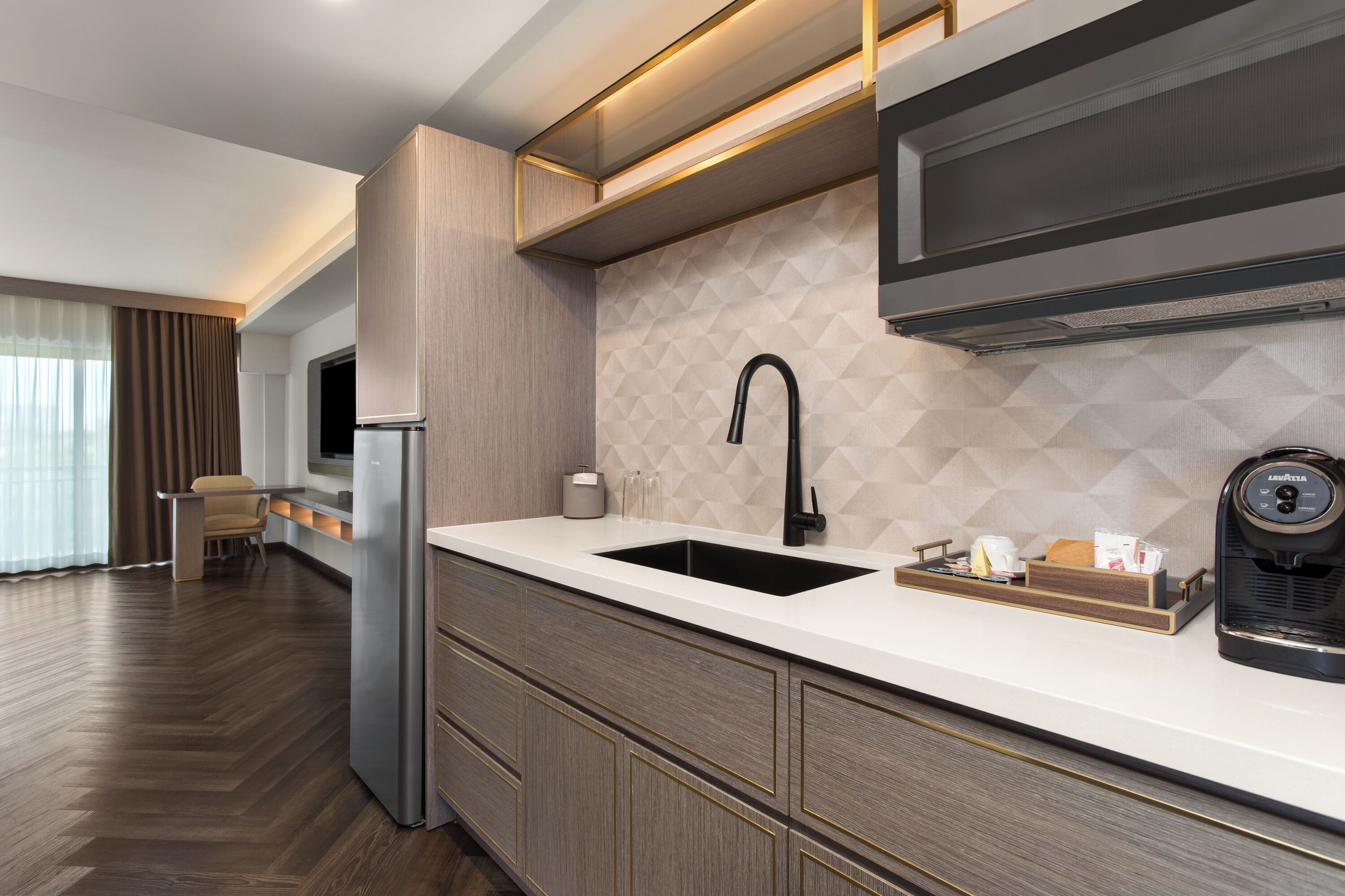 Una cocina moderna con microondas integrado, refrigerador de acero inoxidable y grifo negro.