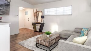 Un salon avec un canapé gris, une table basse et un téléviseur fixé au mur.