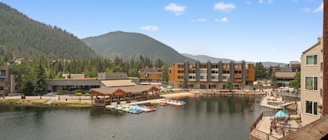 A lakeside view with a dock, boats, and buildings in the background.