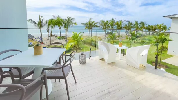 Een balkon met uitzicht op het strand, een tafel met stoelen en een plant in een pot.