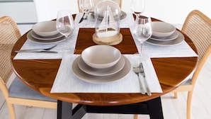 Een eettafel gedekt met borden, glazen en bestek, omringd door rieten stoelen.