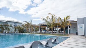 Ein Schwimmbad mit Liegestühlen, Palmen und einer überdachten Sitzgelegenheit.