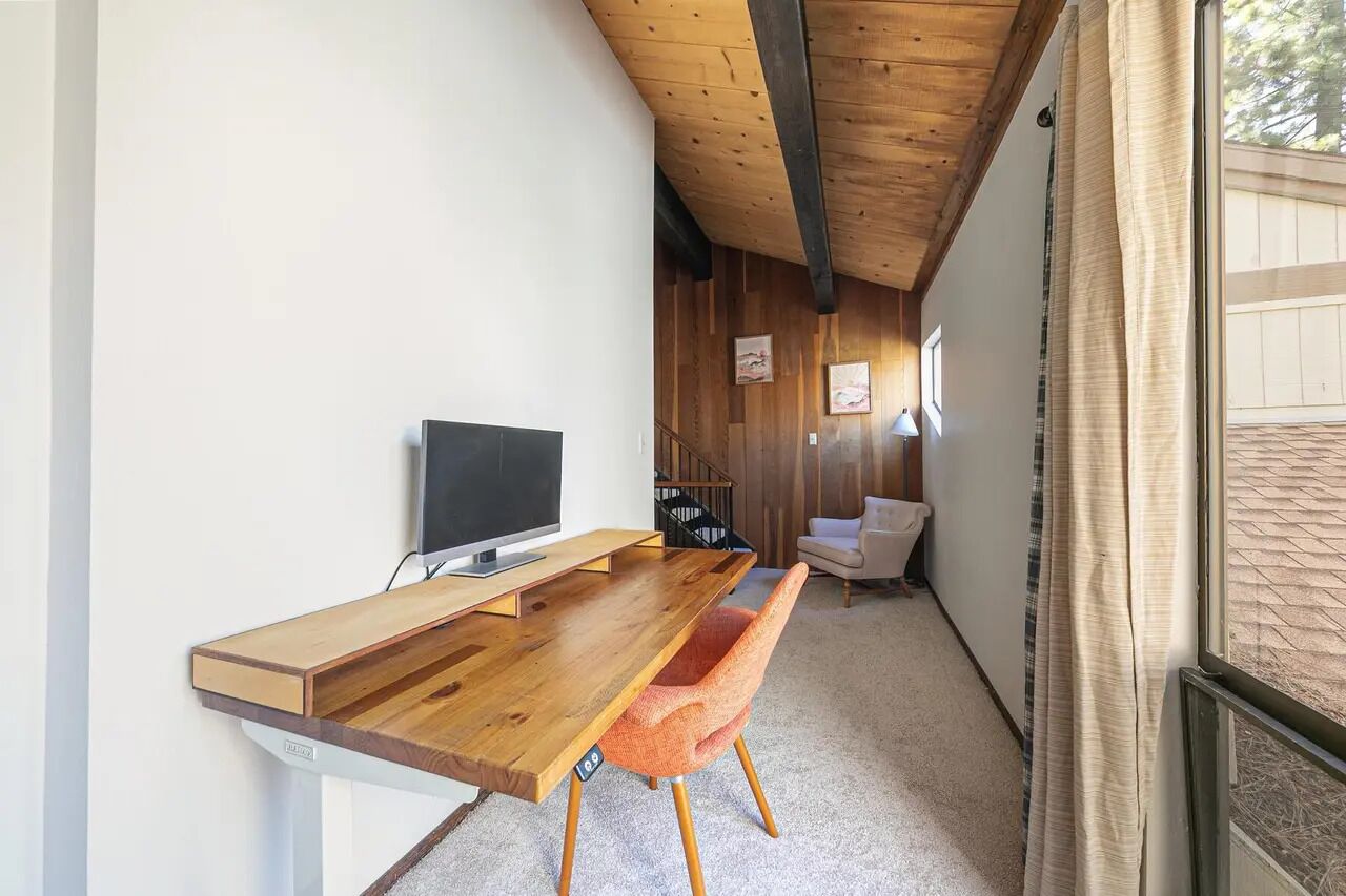 Ein modernes Zimmer mit Schreibtisch aus Holz, einem Fernseher und einem bequemen Sessel.