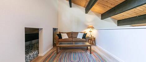 Ein gemütliches Zimmer mit Holzboden, einer Couch mit Kissen, einer Lampe und einem gemusterten Teppich.