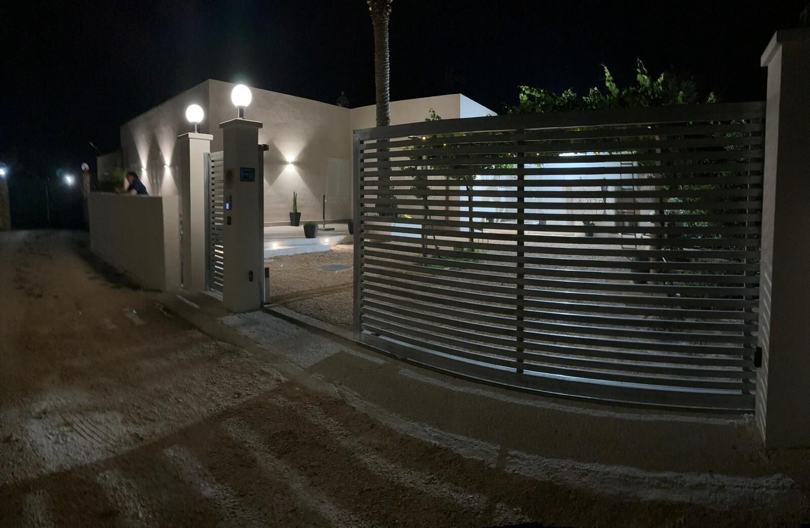 A gated entrance with a modern building, a pathway leading to the entrance, and a security gate.