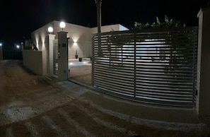 A gated entrance with a modern building, a pathway leading to the entrance, and a security gate. - Stagnone Sunset Holidays (Marsala)