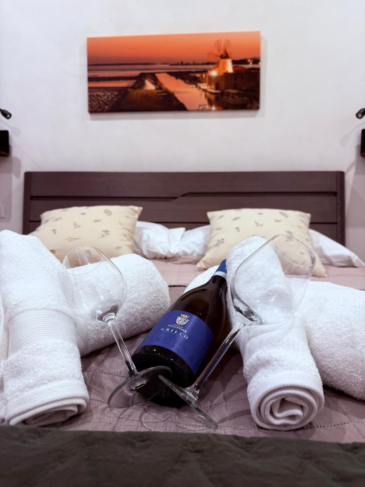 Una cama bien hecha con toallas, una botella de vino y una copa sobre una colcha.