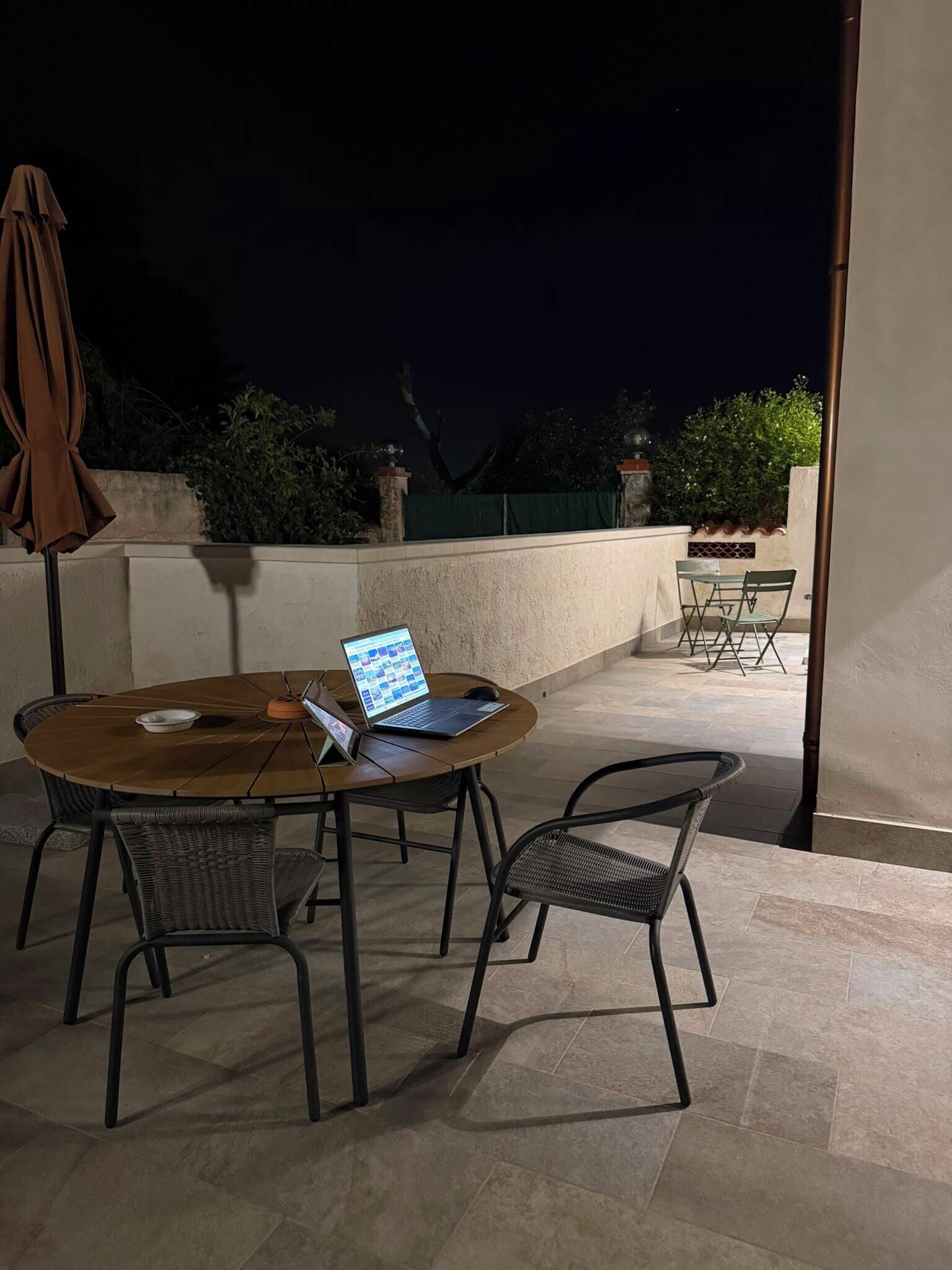 A patio with a round table, two chairs, a laptop, and an umbrella.