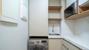 A compact laundry area with a washing machine, a sink, and a microwave. - Condominium With Pool in Downtown Florianopolis - Cjos (Florianópolis)