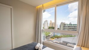 A hotel room with a large window, a bed, and a view of the cityscape. - Condominium With Pool in Downtown Florianopolis - Cjos (Florianópolis)