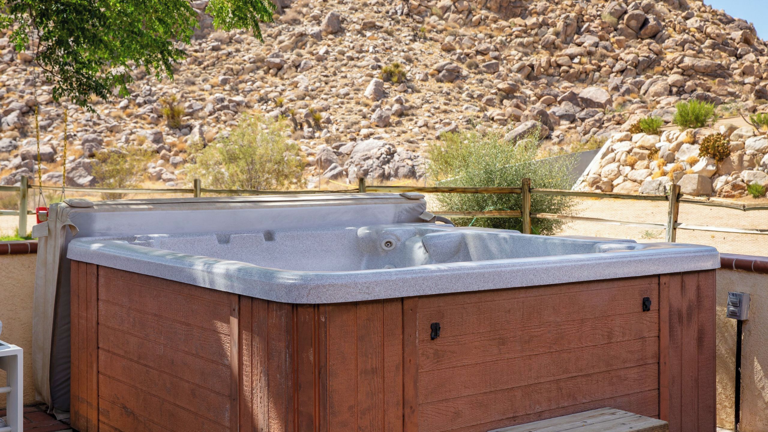 A hot tub with a wooden exterior, set against a rocky landscape with sparse vegetation.