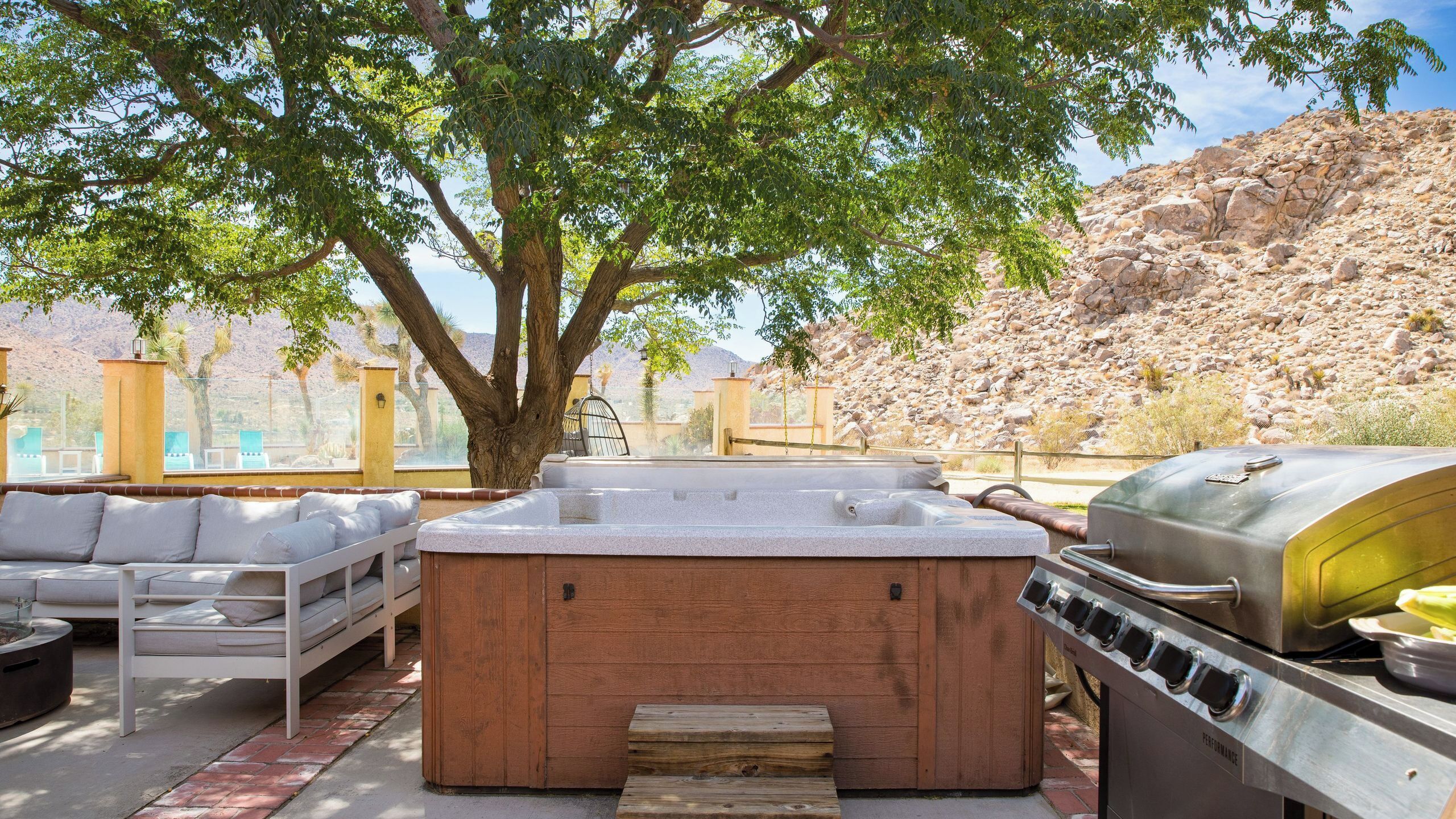 Eine Terrasse mit Whirlpool, Grill und Gartenmöbeln.