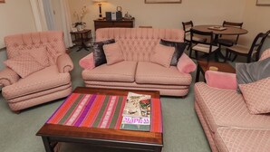 A living room with two pink sofas, a coffee table with magazines, a dining table with chairs, and a lamp. - Grange Cottage (Belford)