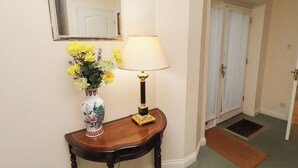 A hallway with a wooden console table, a vase of flowers, a lamp, a mirror, and a door. - Grange Cottage (Belford)