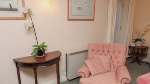 A living room with a pink armchair, a small wooden table with a potted plant, and two framed artworks on the wall. - Grange Cottage (Belford)