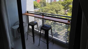 A balcony with two black stools, a white radiator, and a view of buildings and trees. - Back to the Neighborhood - Luminous Studio in South Neighborhood with Pool (San Miguel de Tucumán)