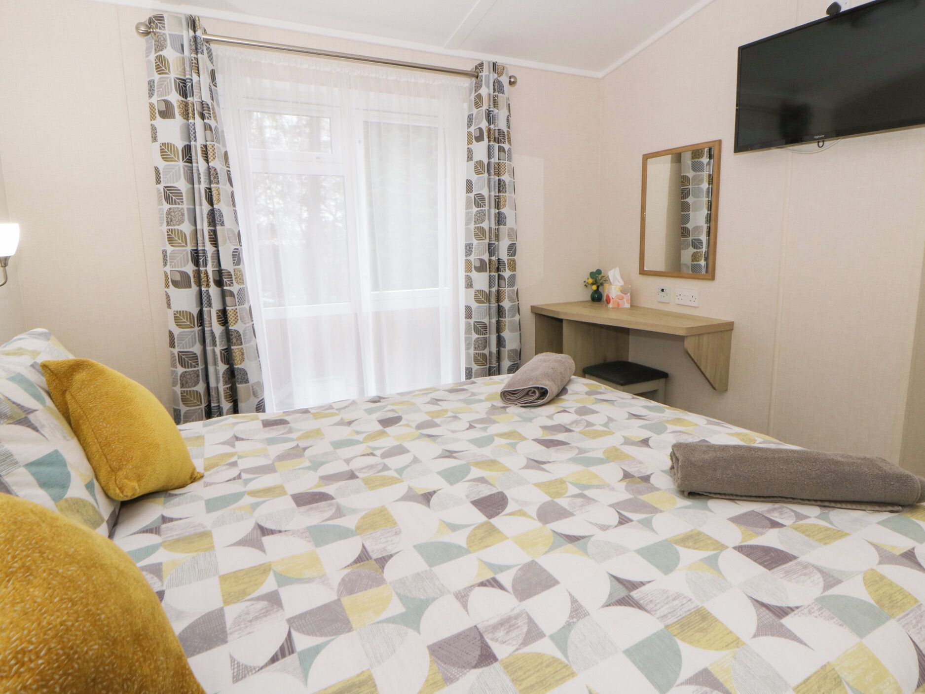 A hotel room with a bed, a desk, a mirror, and a TV.