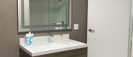 A bathroom with a large mirror, a white sink, a towel rack, and a door.