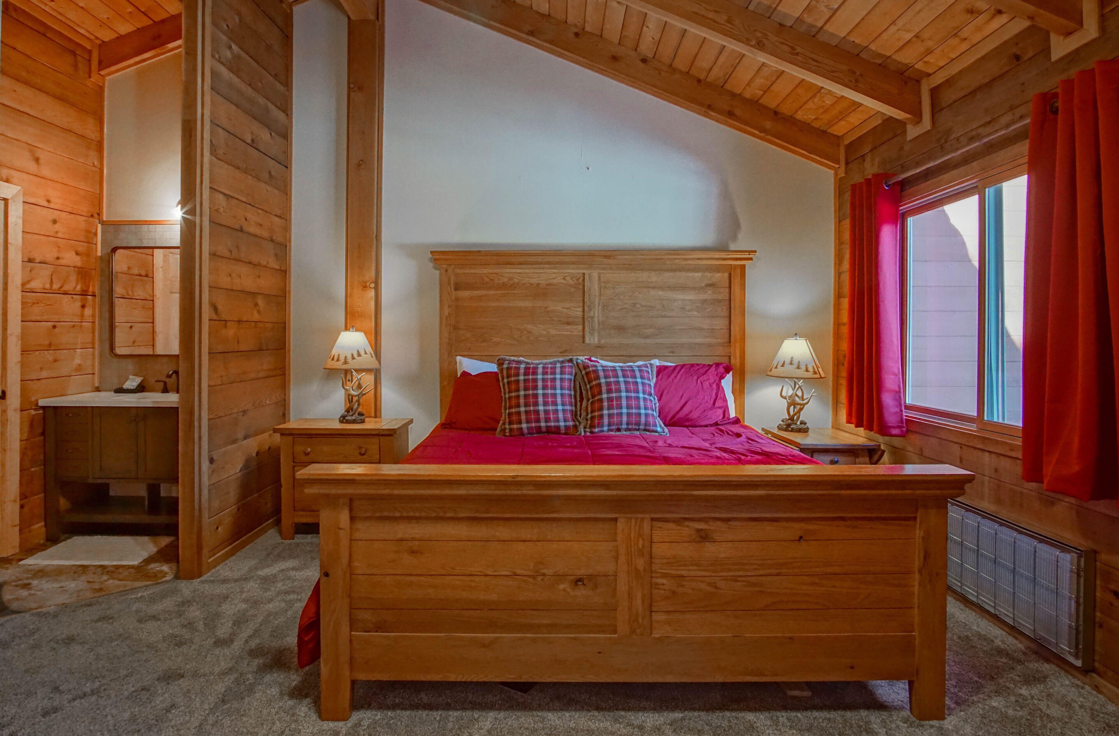 A wooden bedroom with a bed, two bedside tables, and a window with red curtains.