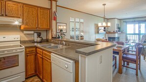 A kitchen with wooden cabinets, a dishwasher, a stove, and a dining area with a table and chairs. - 2 Br: Snowcrest 214a 2 Bedroom: Indoor Hot Tubs Game Room Easy Slope Access (Snowshoe)
